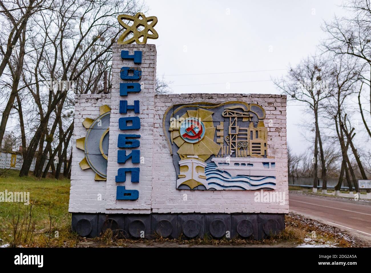 Chernobyl, Ukraine - August 2019 A sign with the name of Chernobyl written in Ukrainian. On top of the monument there is a yellow atom. On the side th Stock Photo