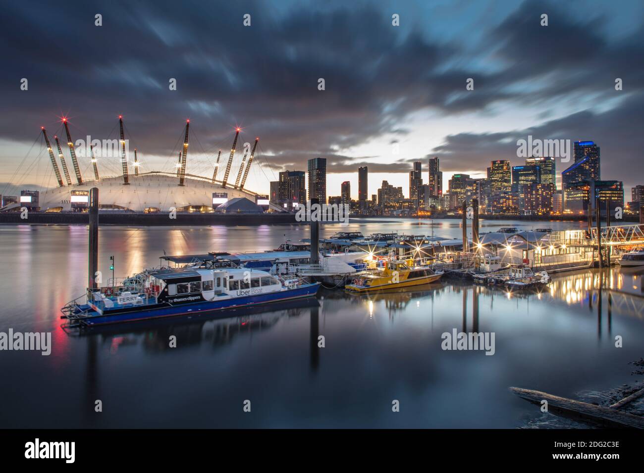 London, skyline of Docklands Canary Wharf commercial centre, O2 concert arena & events venue, river boats on the Thames, dusk, illuminated buildings Stock Photo