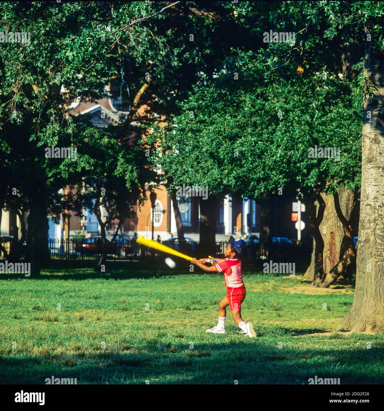 New York 1985, Little African American boy playing baseball, swinging baseball bat, Battery park, lower Manhattan, New York City, NY, NYC, USA, Stock Photo