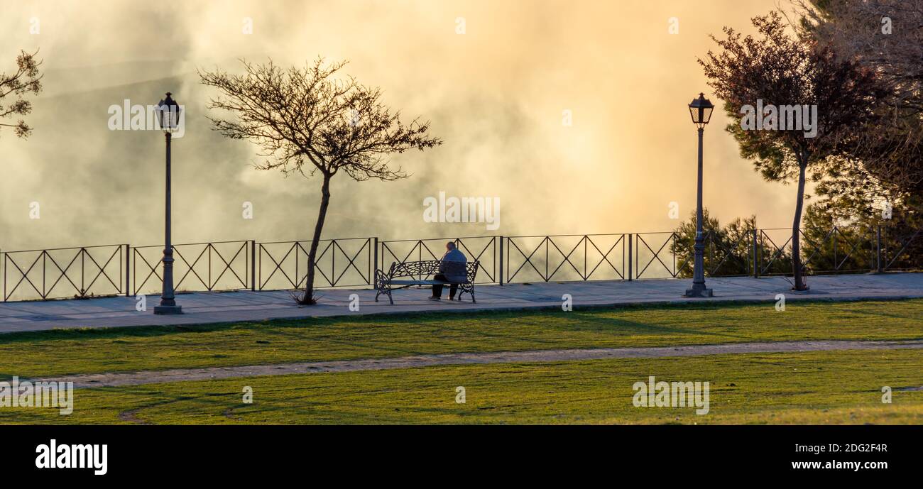 Silhouette of a man sitting on a park bench in a dramatic winter sunset ...