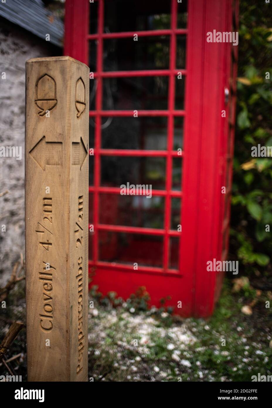 Wooden Sign post marking directions on South West Coastal footpath in front of red telephone box in Devon village of Bucks Mills Stock Photo