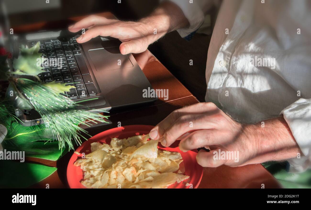 The hands of a man working on his computer. He is at home, surrounded by decorations for the holidays to come. He is indulging himself a treat. Stock Photo