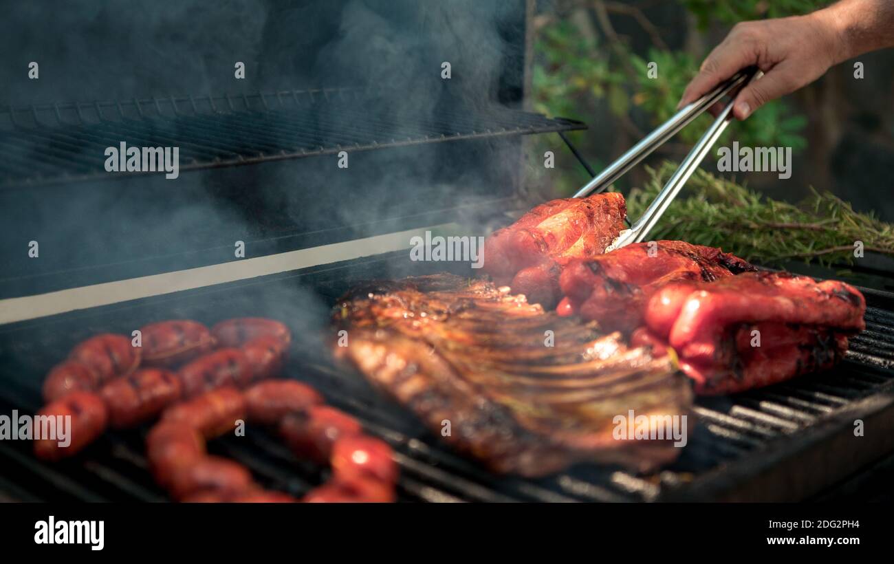 https://c8.alamy.com/comp/2DG2PH4/hand-of-man-with-metal-tong-cooking-pork-ribs-with-red-peppers-on-bbq-grill-cook-a-delicious-grilled-meat-food-cooked-with-grilling-barbecue-chef-c-2DG2PH4.jpg