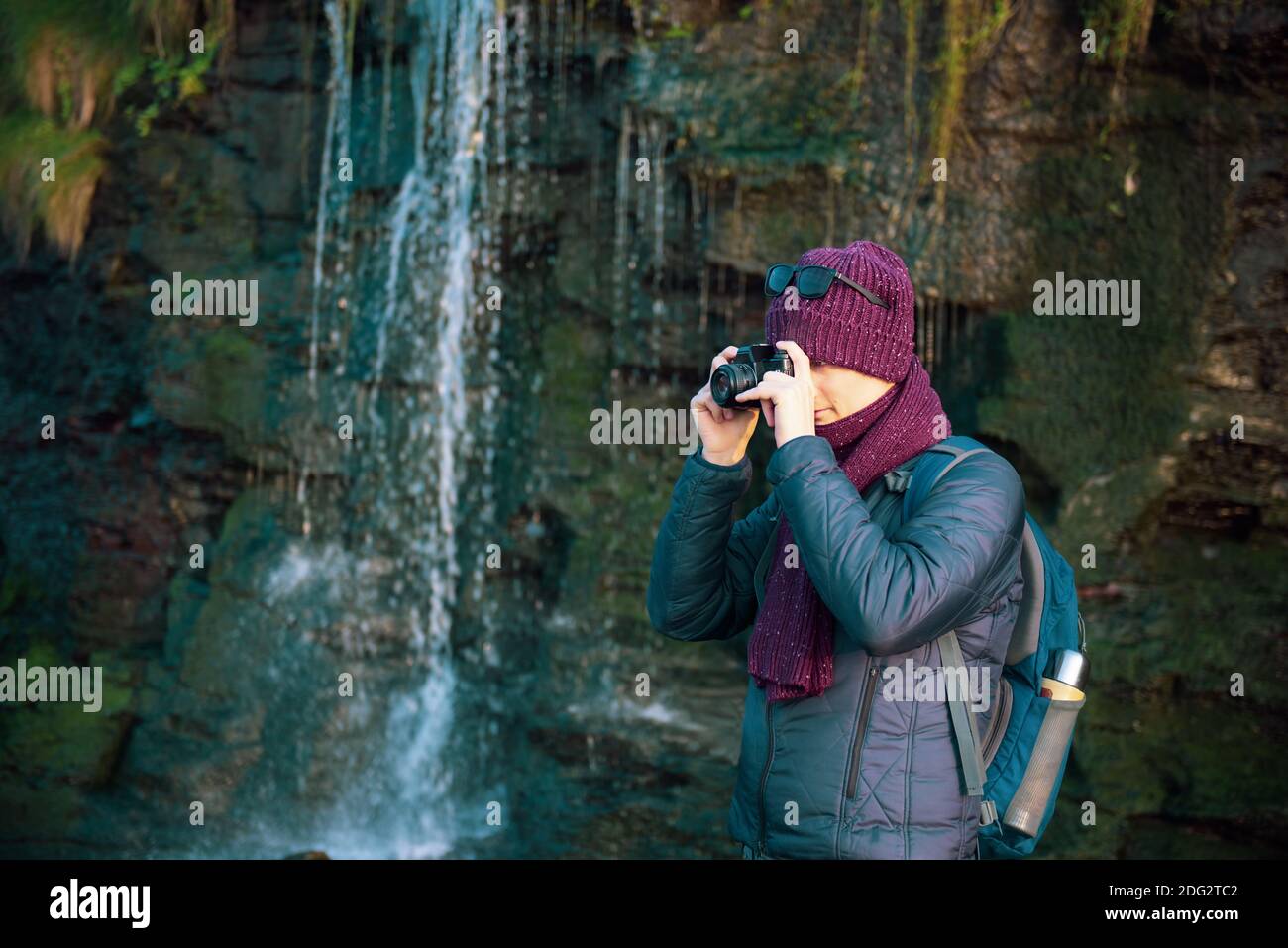 Young Man taking picture by analog camera during his walk near waterfall. Local self-traveling in autumn, winter. Hobby concept. Selective focus. Copy Stock Photo
