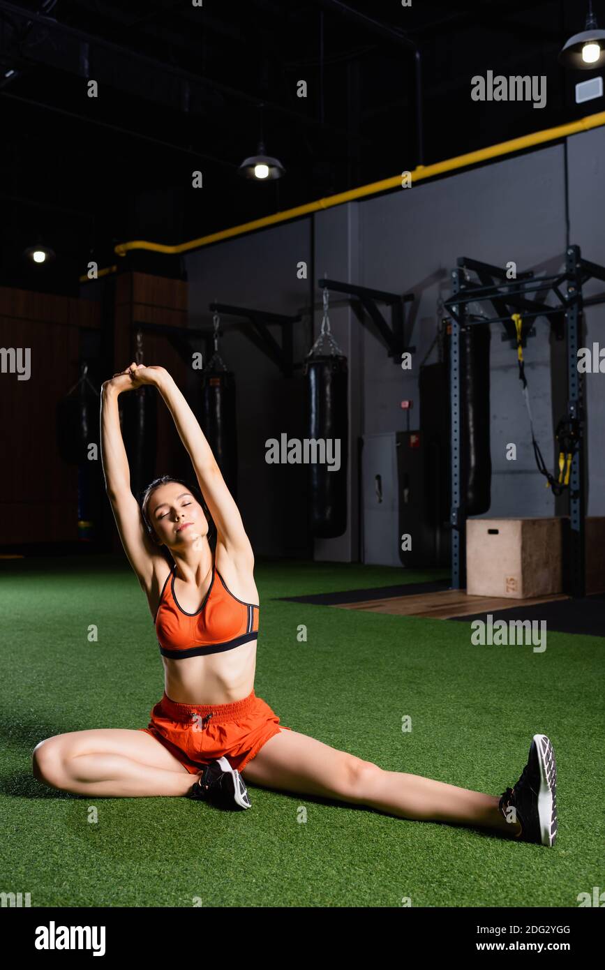 sportswoman in top and shorts stretching hands with closed eyes in gym Stock Photo
