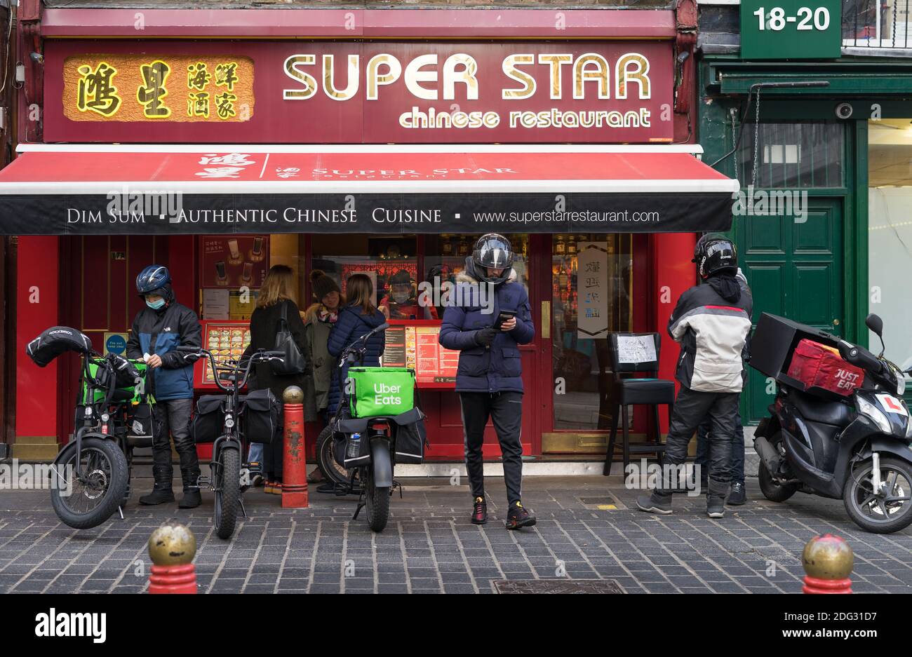 Uber Eats and Just Eat bike delivery riders wait outside a Chinese restaurant in Chinatown. London Stock Photo