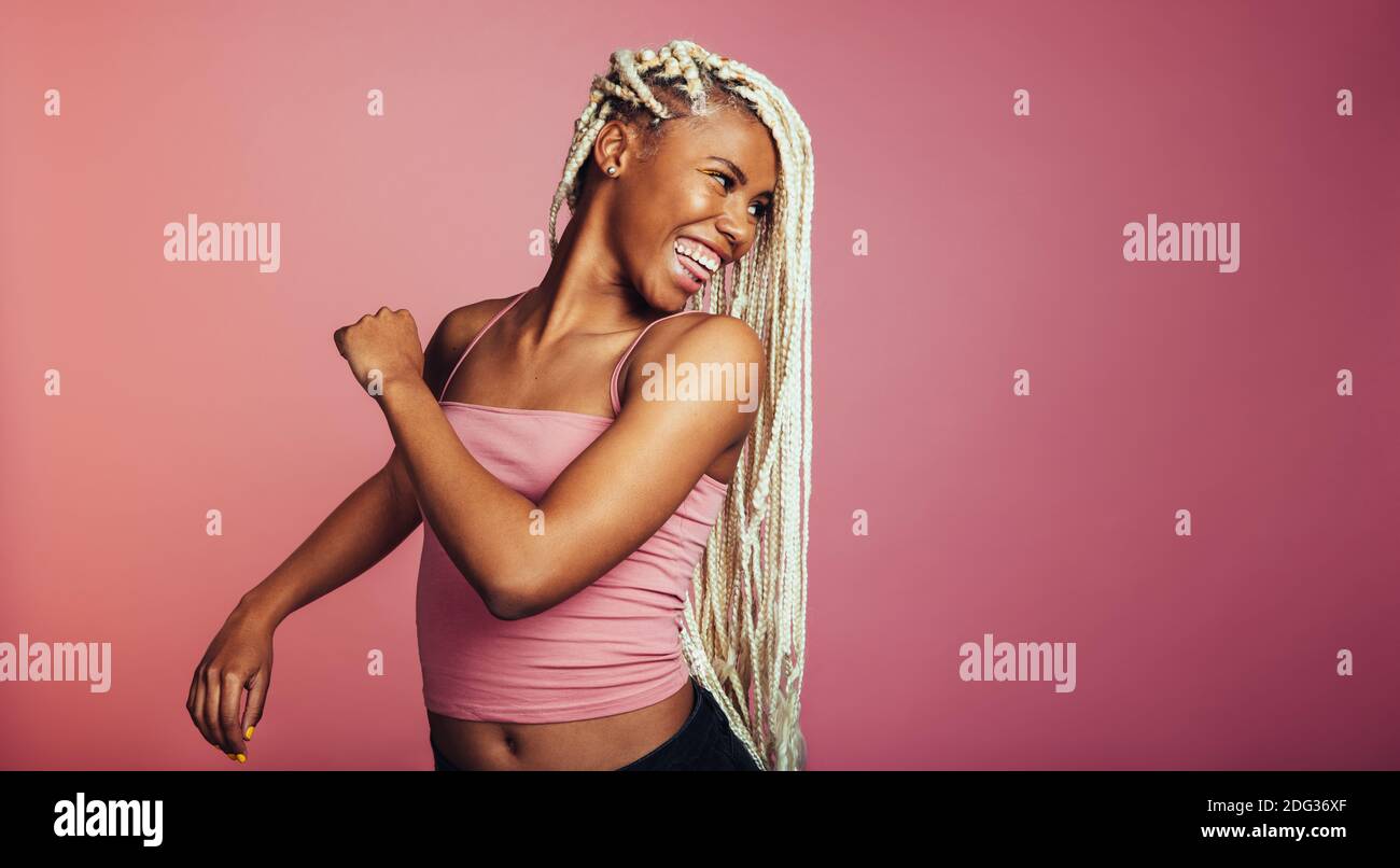 Close up of smiling woman looking back over her shoulder. African american woman with braided hair on pink background. Stock Photo