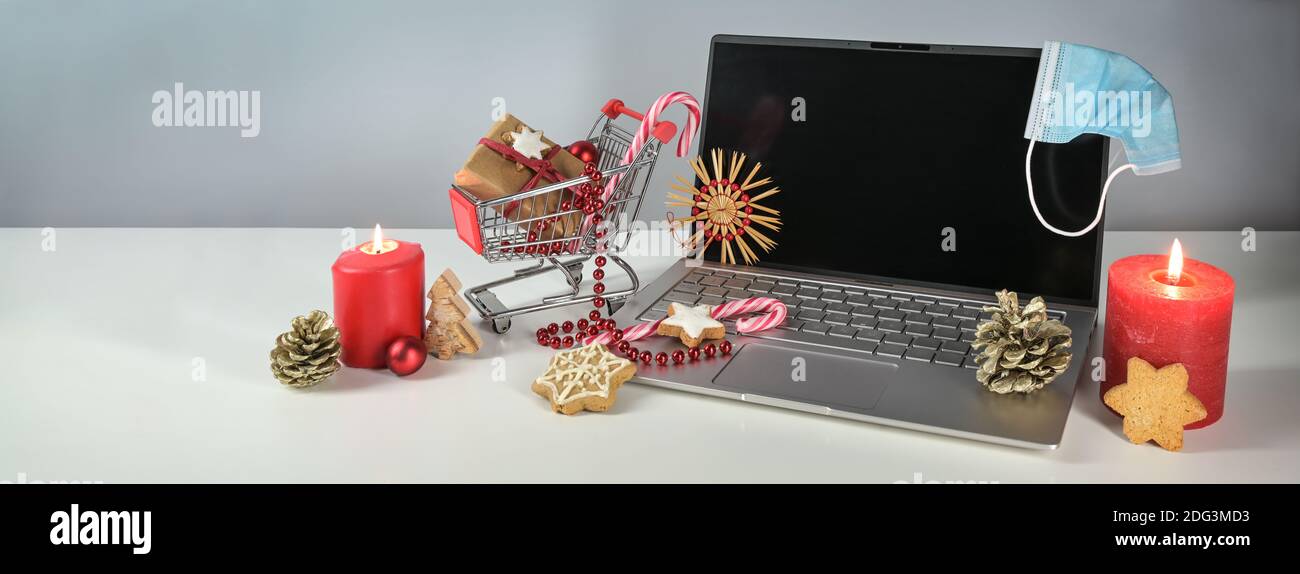 Holiday online shopping during coronavirus pandemic, laptop, surgical face mask against covid-19 pandemic, burning candles, Christmas  decoration and Stock Photo