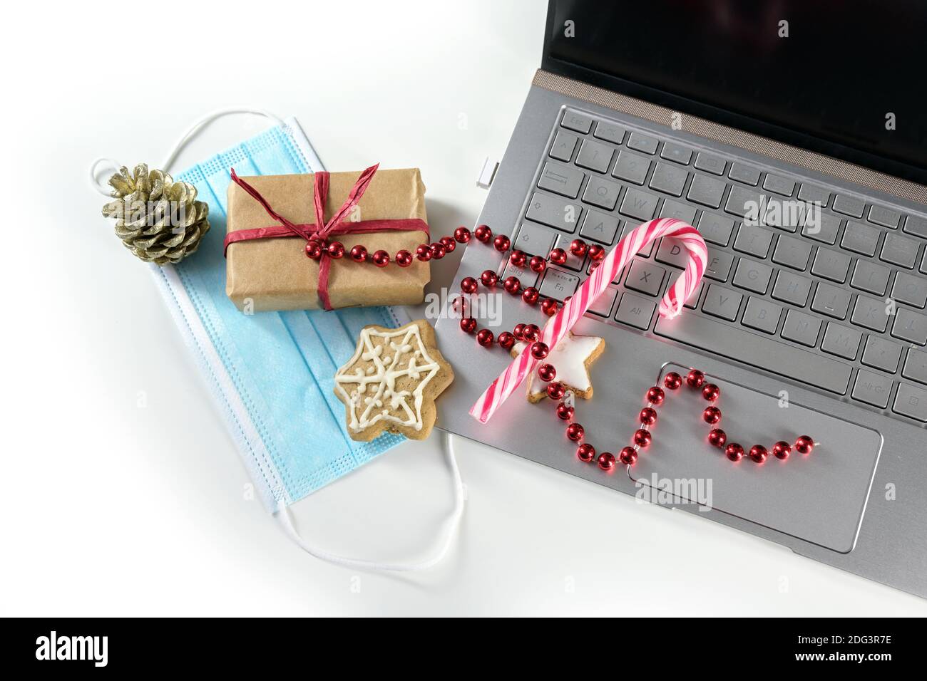 Online shopping for Christmas during coronavirus  pandemic, laptop with protective face mask, gift, sweets and holiday decoration on a white backgroun Stock Photo