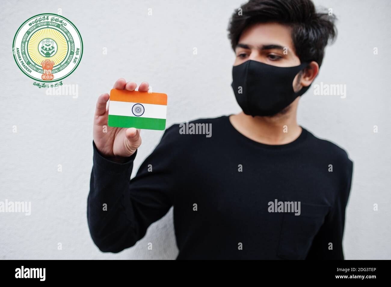 Indian man wear all black and face mask, hold India flag in hand isolated on white background with Andhra Pradesh state emblem . Coronavirus India sta Stock Photo