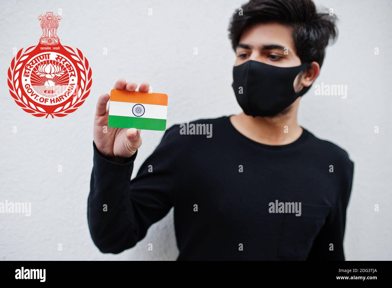 Indian man wear all black and face mask, hold India flag in hand isolated on white background with Haryana state emblem . Coronavirus India states and Stock Photo