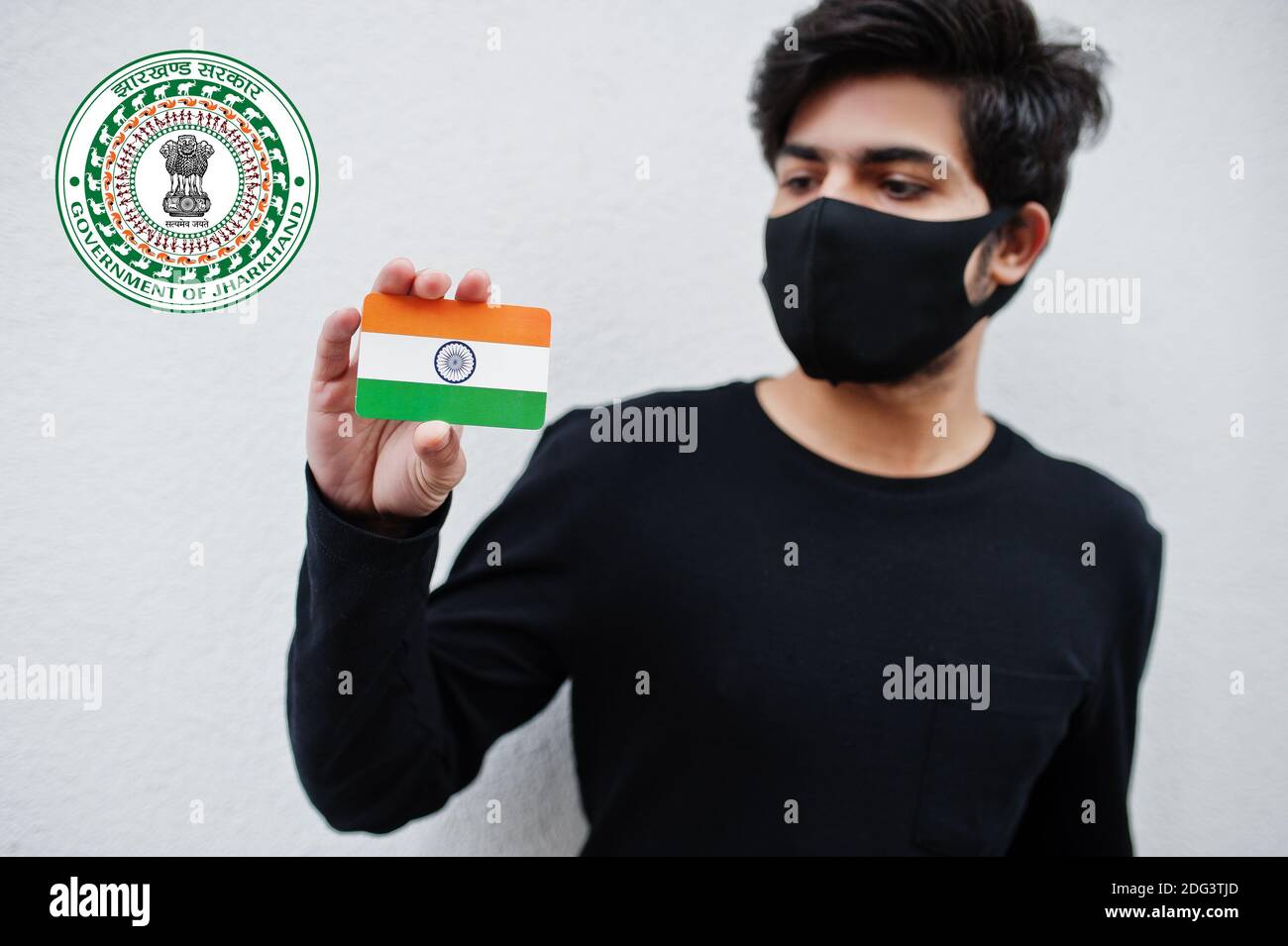 Indian man wear all black and face mask, hold India flag in hand isolated on white background with Jharkhand state emblem . Coronavirus India states a Stock Photo