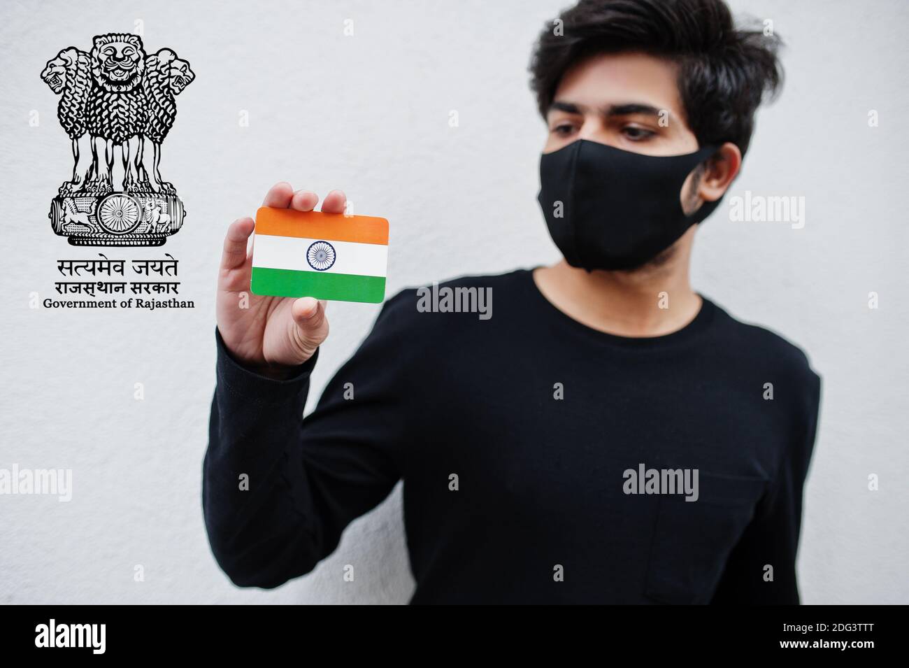 Indian man wear all black and face mask, hold India flag in hand isolated on white background with Rajasthan state emblem . Coronavirus India states a Stock Photo