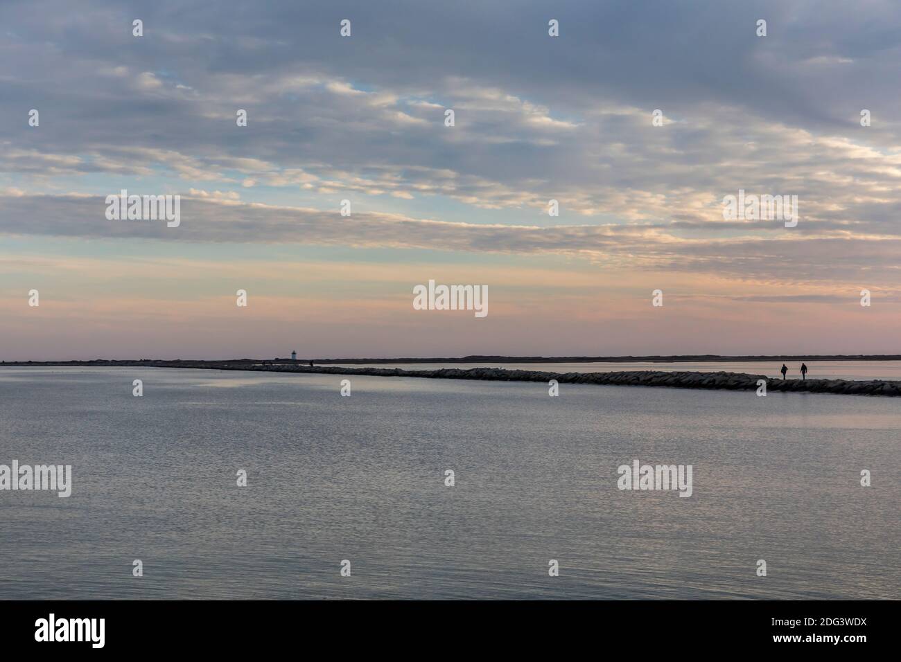 Silhouetted people walking at Provincetown breakwater at sunset Stock