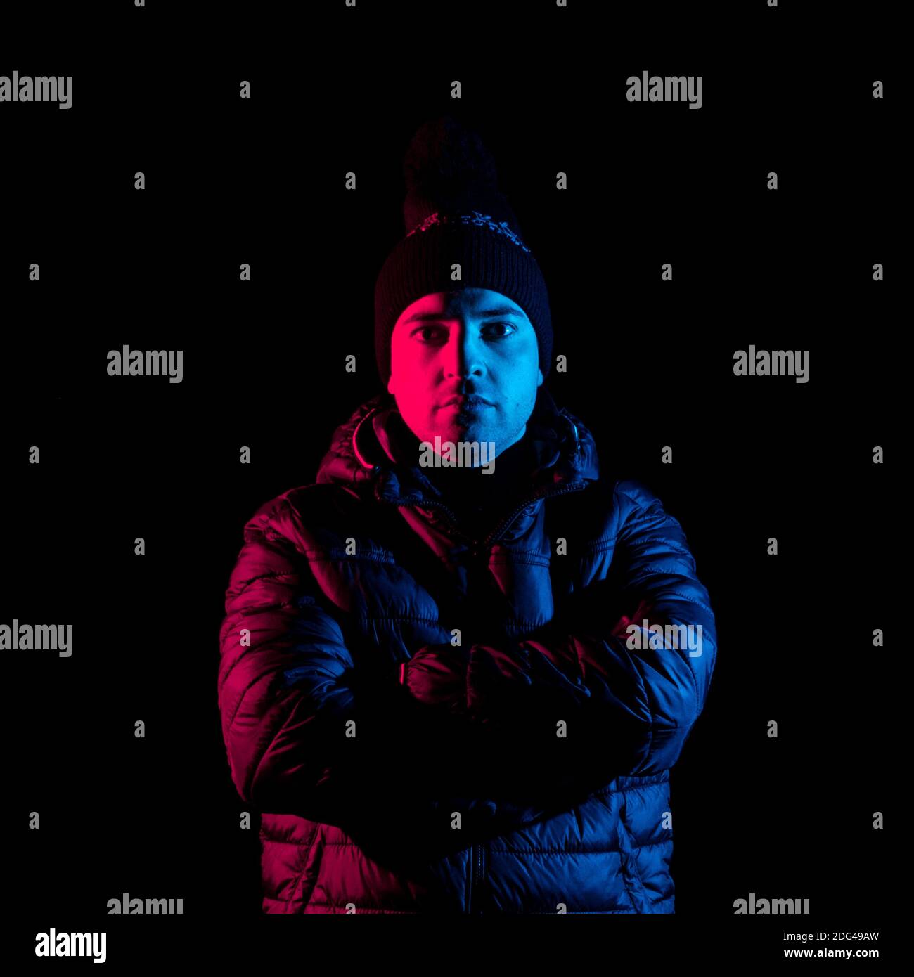 A closeup of a male wearing a thick jacket folding his arms across his chest on a black background Stock Photo