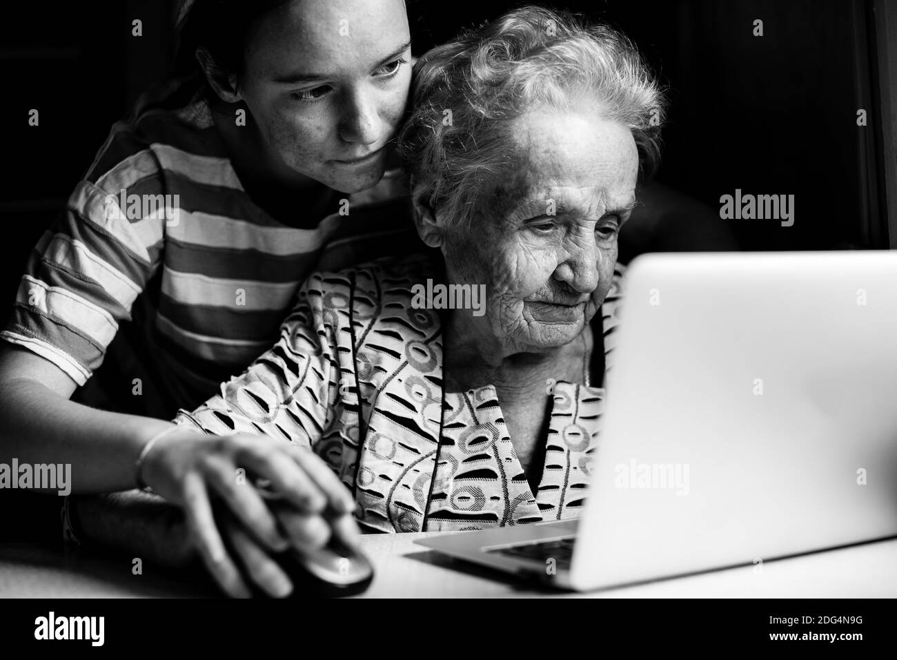 Teen girl teaches her grandmother to work on the computer laptop. Black and white photo. Stock Photo