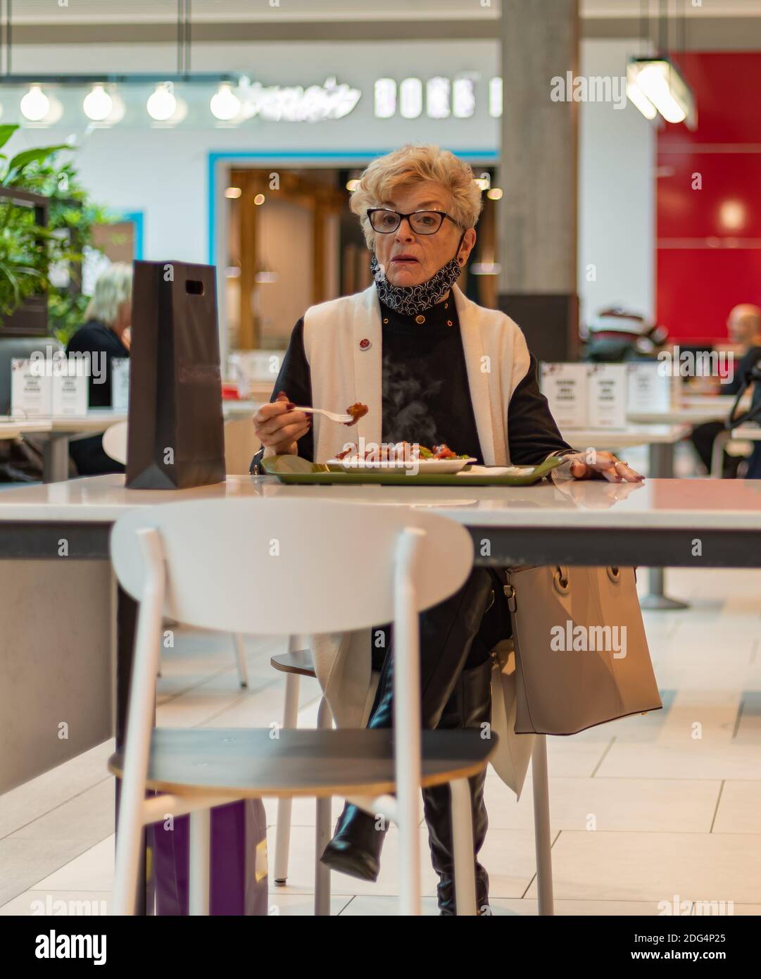 Portrait of the senior woman with protective mask sitting in the cafeteria and having her lunch. Selective focus, street view. Langley, BC, Canada-Nov Stock Photo