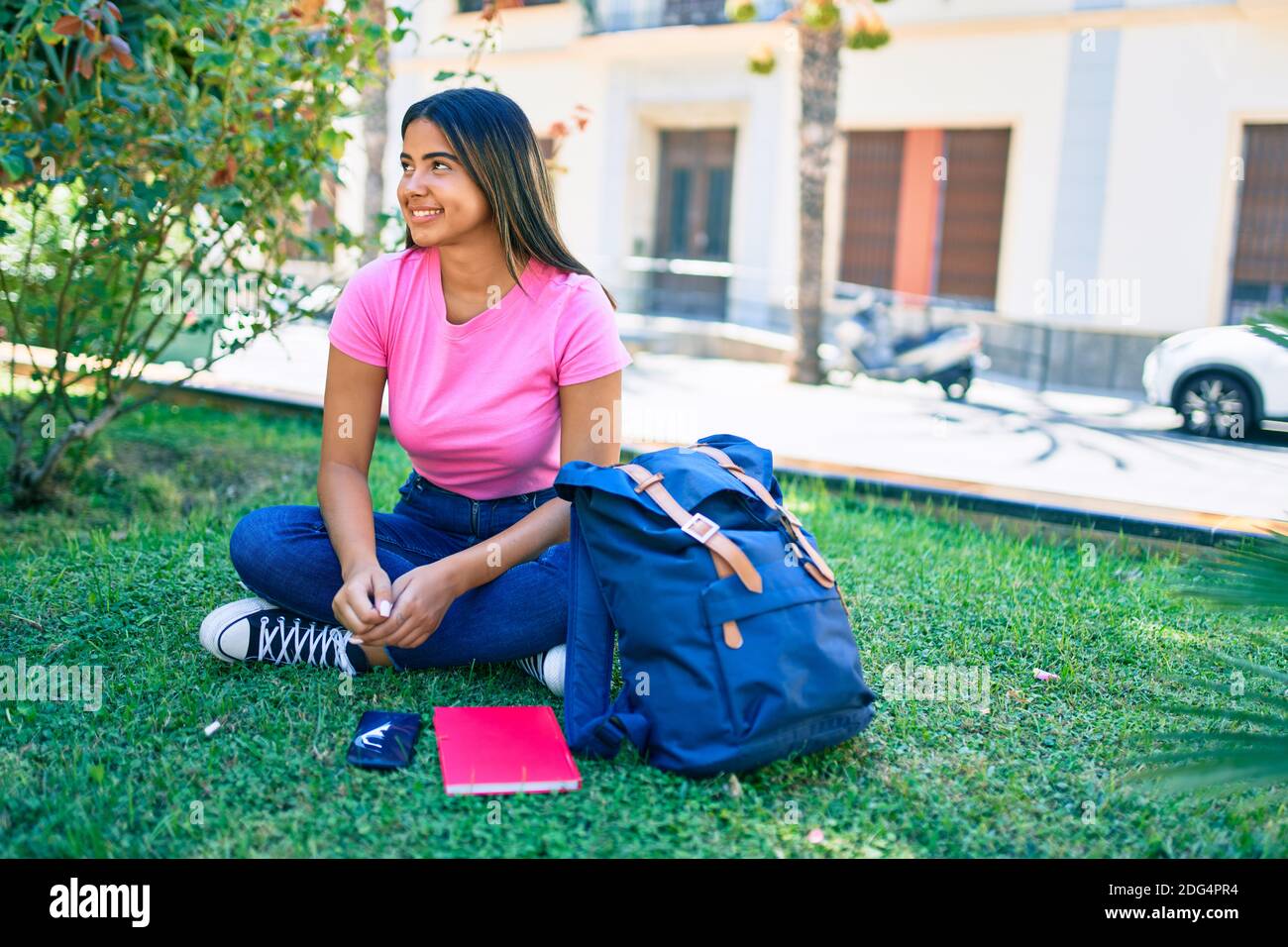 Young latin student girl smiling happy sitting on the grass at ...