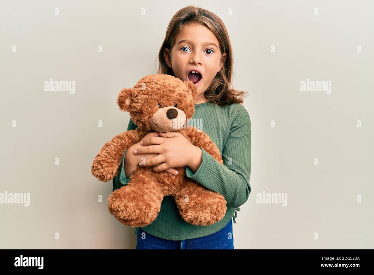 Little beautiful girl hugging teddy bear afraid and shocked with
