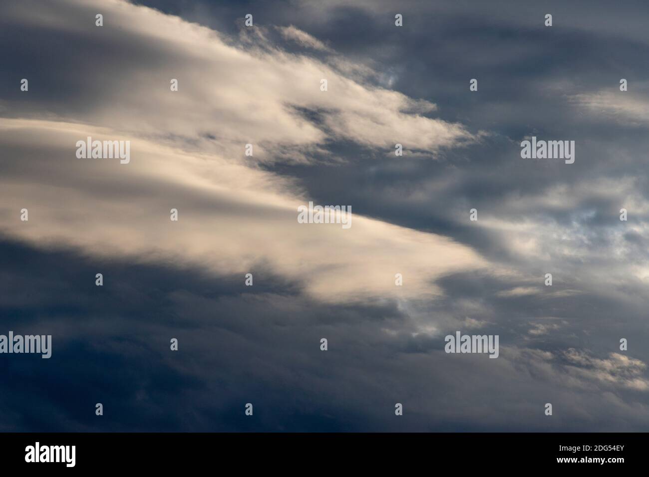 As a storm builds, layered stratus clouds are illuminated by a setting November sun Stock Photo