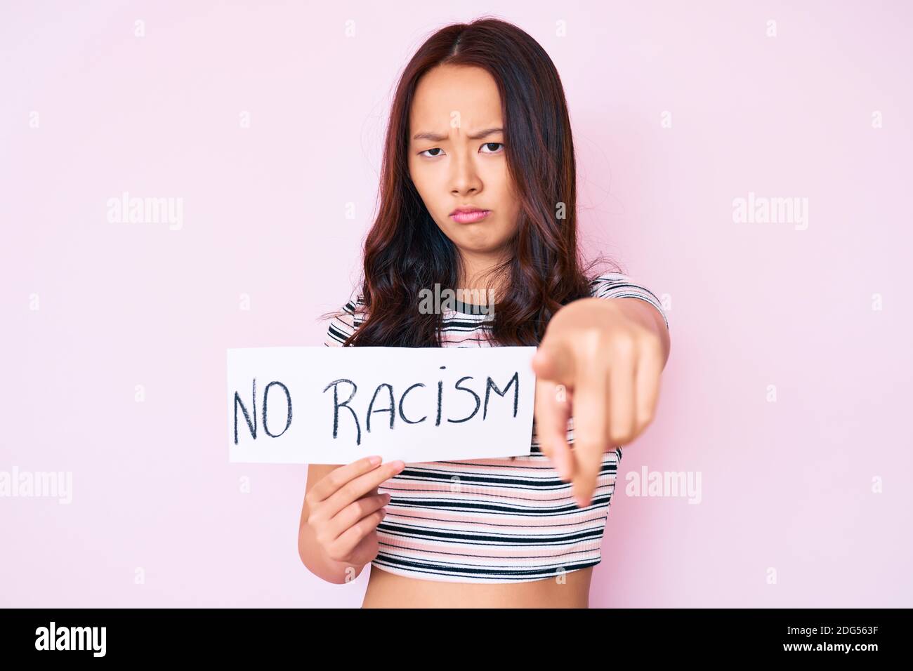 Young beautiful chinese girl holding no racism banner pointing with finger to the camera and to you, confident gesture looking serious Stock Photo
