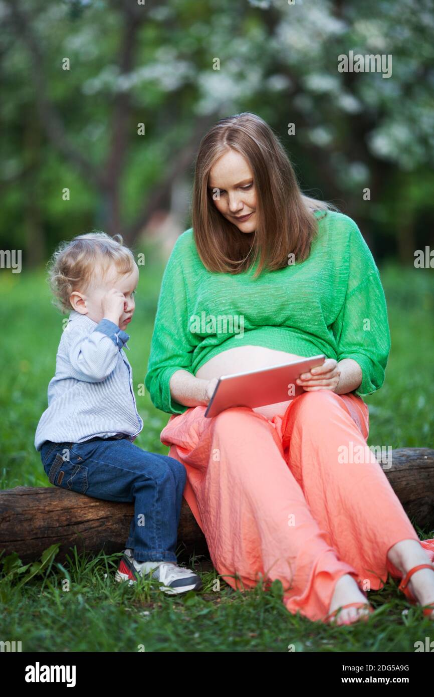 Pregnant mother with little son using touch pad in the park Stock Photo