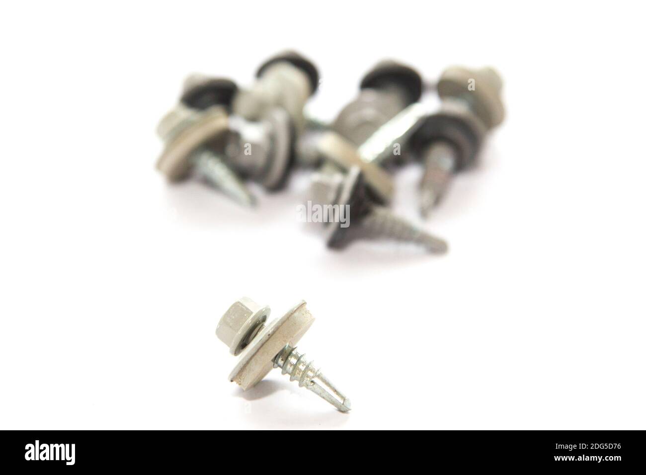 metal screw in close-up with pile of screws out of focus background on white background Stock Photo