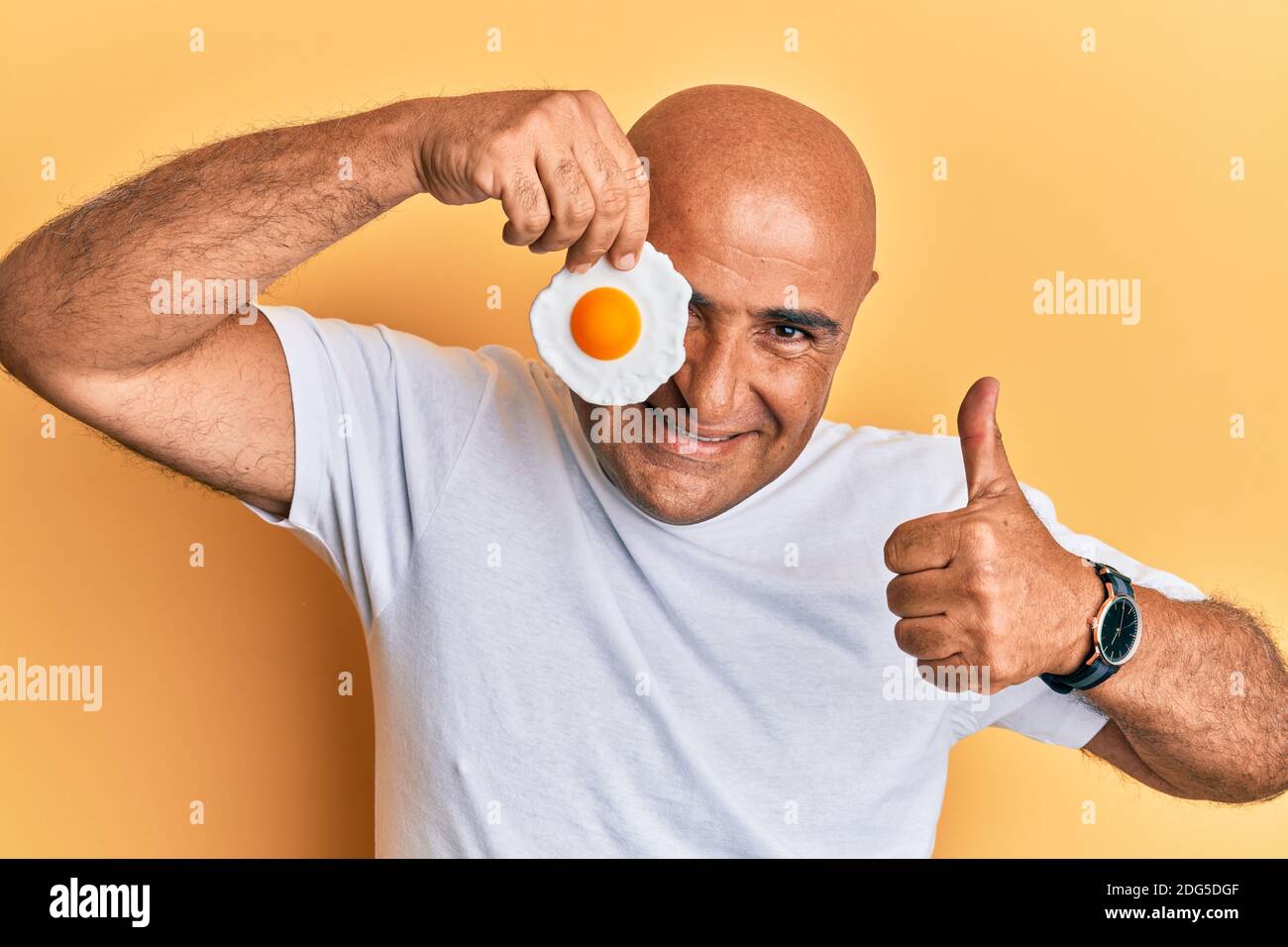 Mature middle east man holding fried egg smiling happy and positive ...