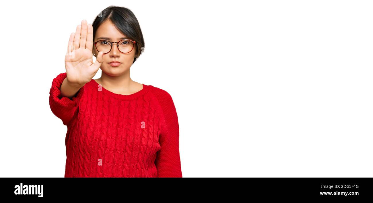 Young beautiful hispanic woman with short hair wearing casual sweater and glasses doing stop sing with palm of the hand. warning expression with negat Stock Photo