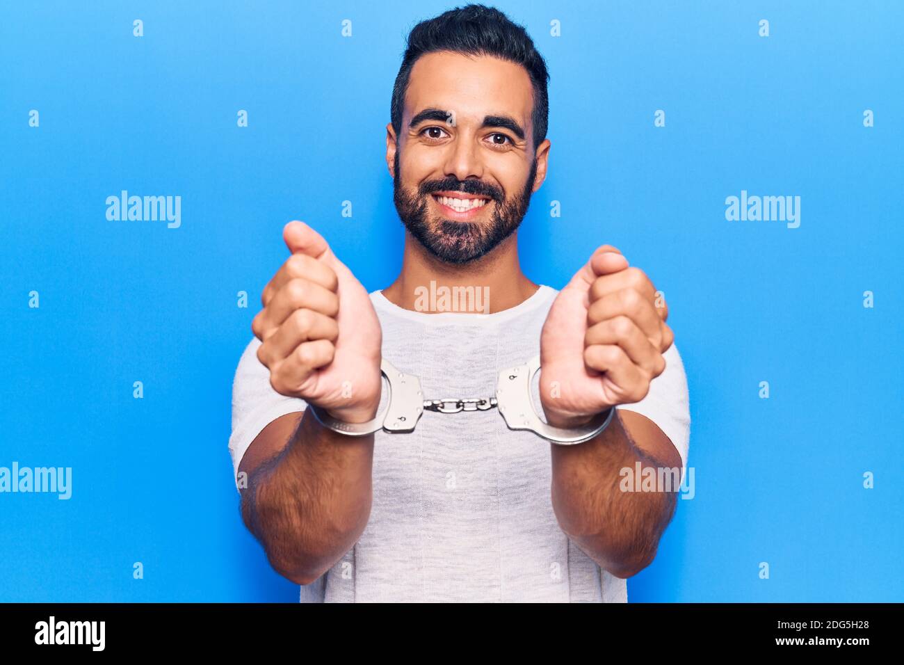 Young hispanic man wearing prisoner handcuffs looking positive and happy standing and smiling with a confident smile showing teeth Stock Photo