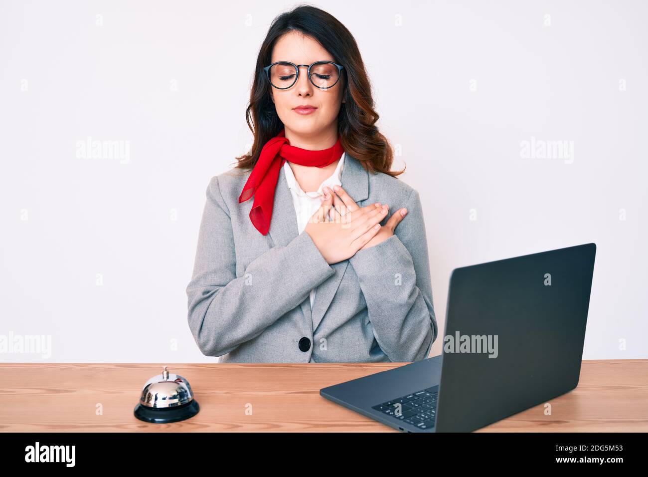 Young beautiful brunette woman working at hotel reception using laptop ...