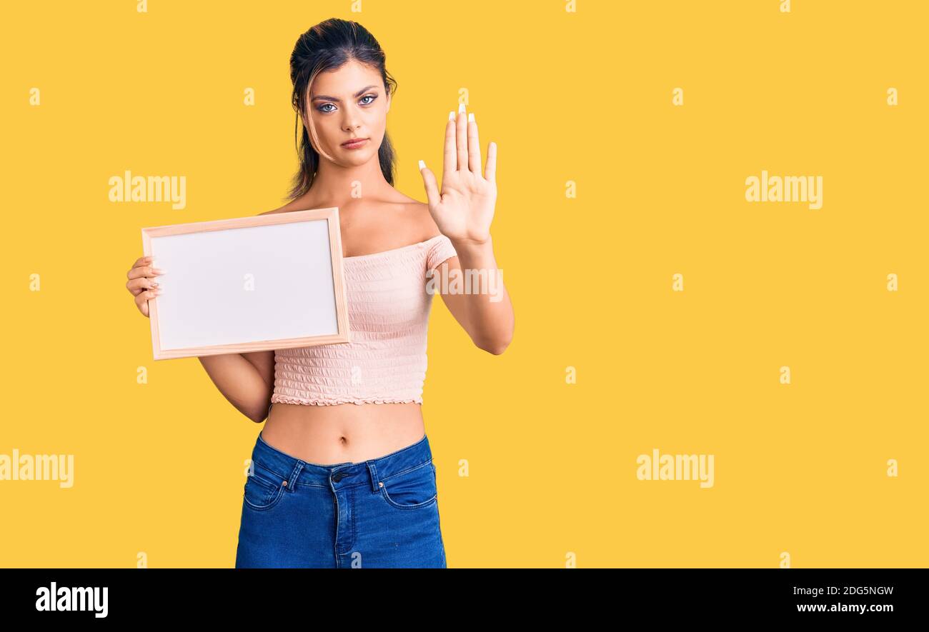 Young beautiful woman holding empty white chalkboard with open hand doing stop sign with serious and confident expression, defense gesture Stock Photo