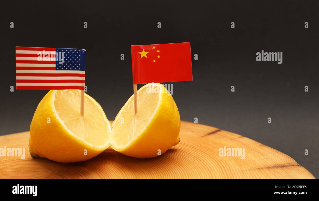 US American and Chinese flags poking out of a sliced lemon on a chopping block representing the strained soured relationship and trade war being waged Stock Photo