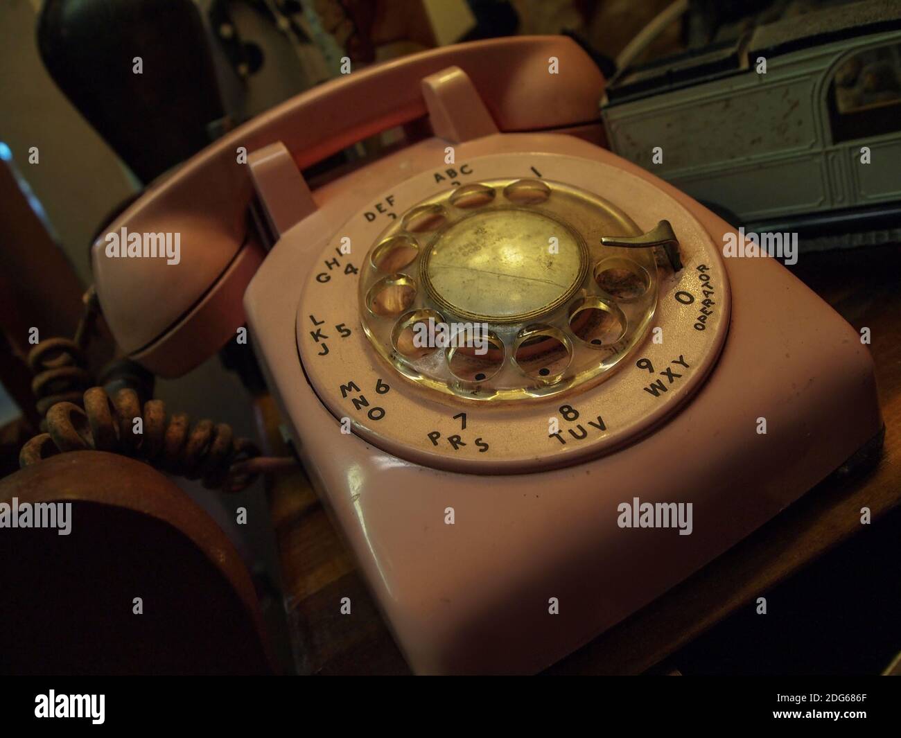 A worn, dirty old vintage pink telephone is nestled among other forgotten artifacts of the 1900s in a dark room. Stock Photo