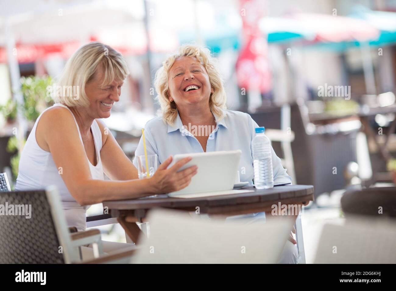 Senior women laughing while using tablet PC in cafe Stock Photo