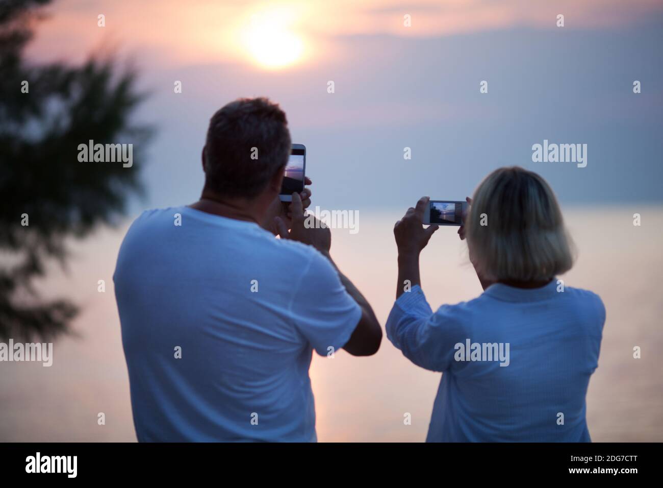 Back view of couple taking photos of sunset Stock Photo