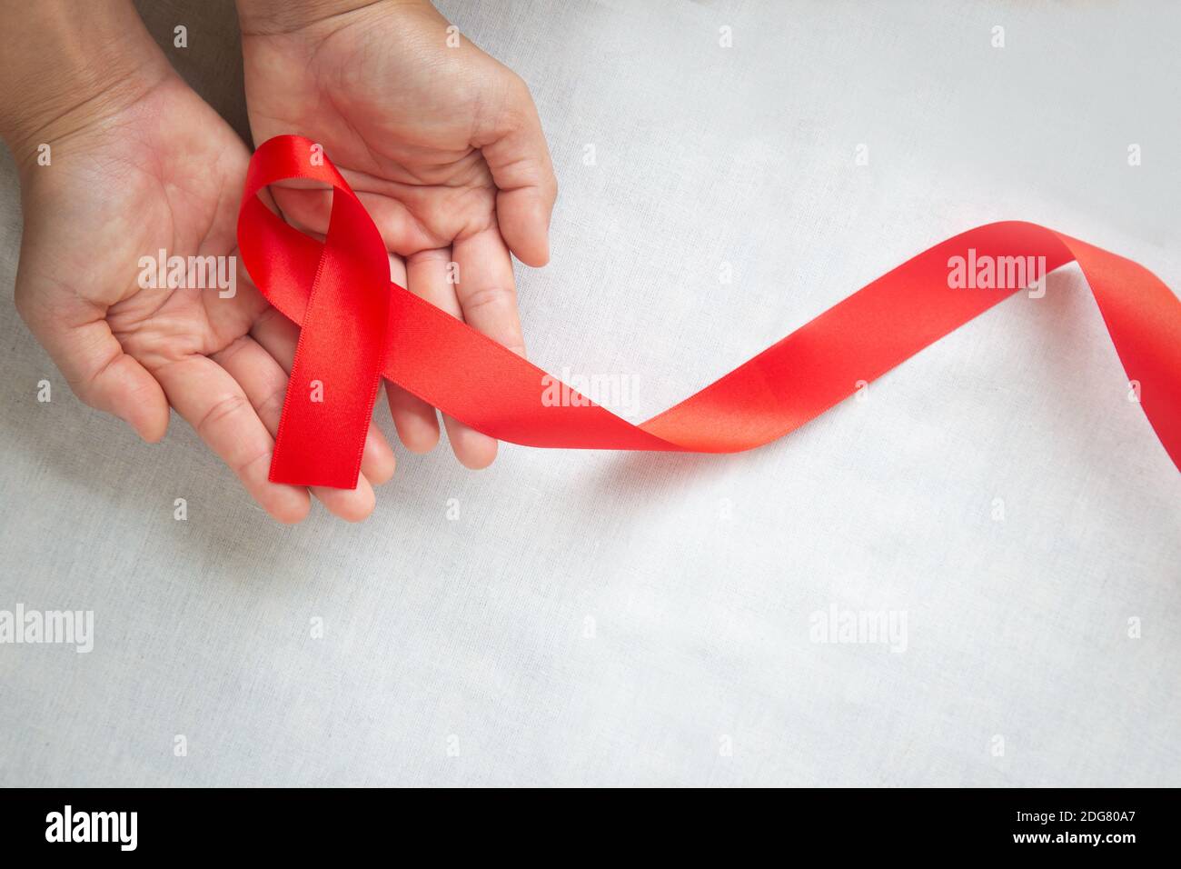 Hand holding Red ribbon on white background with copy space, the solidarity of people living with HIV, AIDS symbol, and for the awareness and preventi Stock Photo