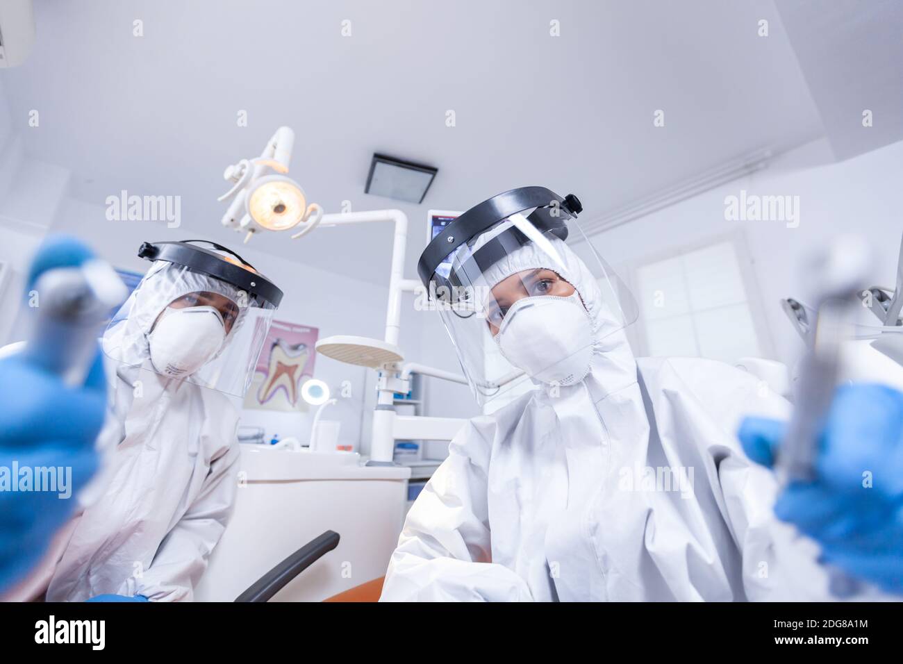 Patient pov of orthodontist and assistan doing procedure for mouth hygine in coverall. Stomatology team wearing safety equipment against coronavirus treating patient. Stock Photo