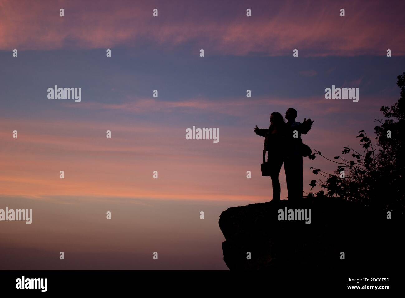 A young couple's silhouette after the sunset holding hands up in the air Stock Photo