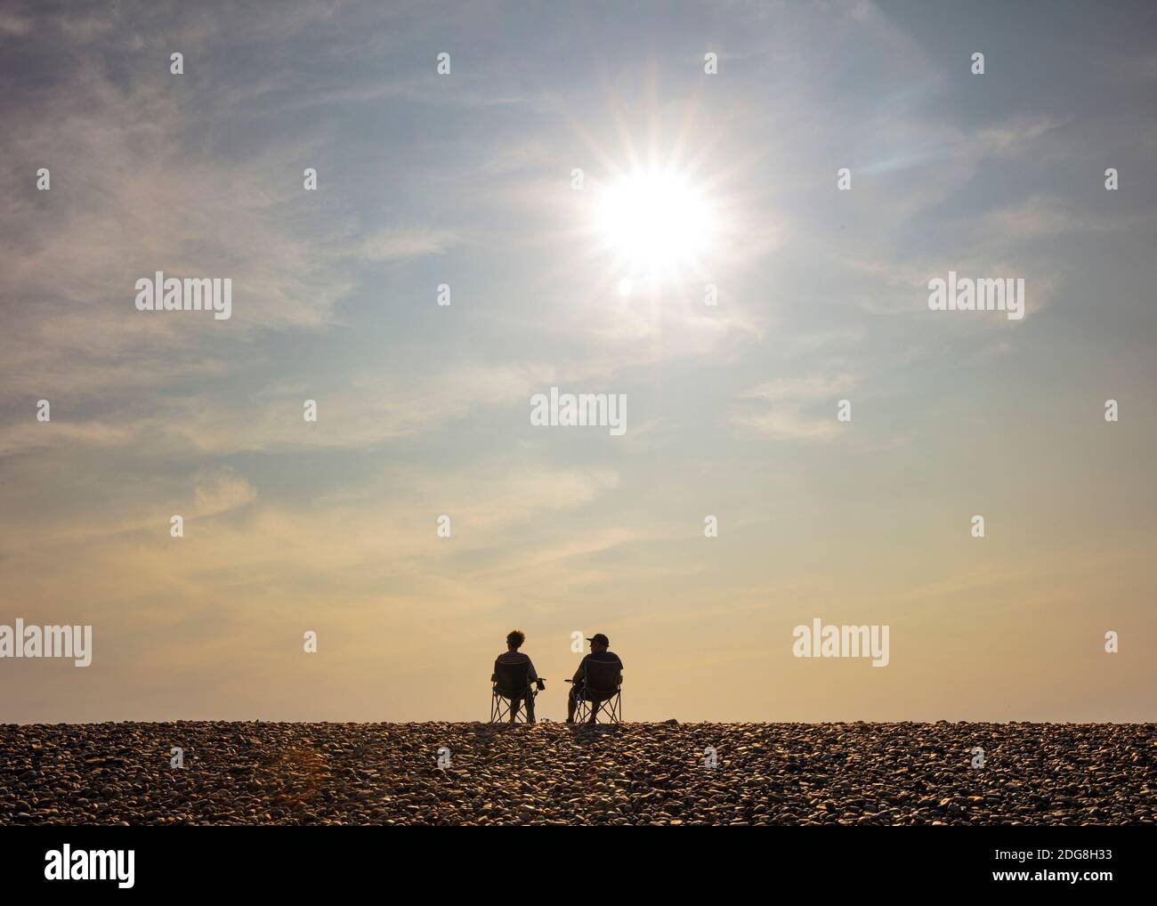 A couple in silhouette, sitting, relaxing on a beach under a full sun Stock Photo