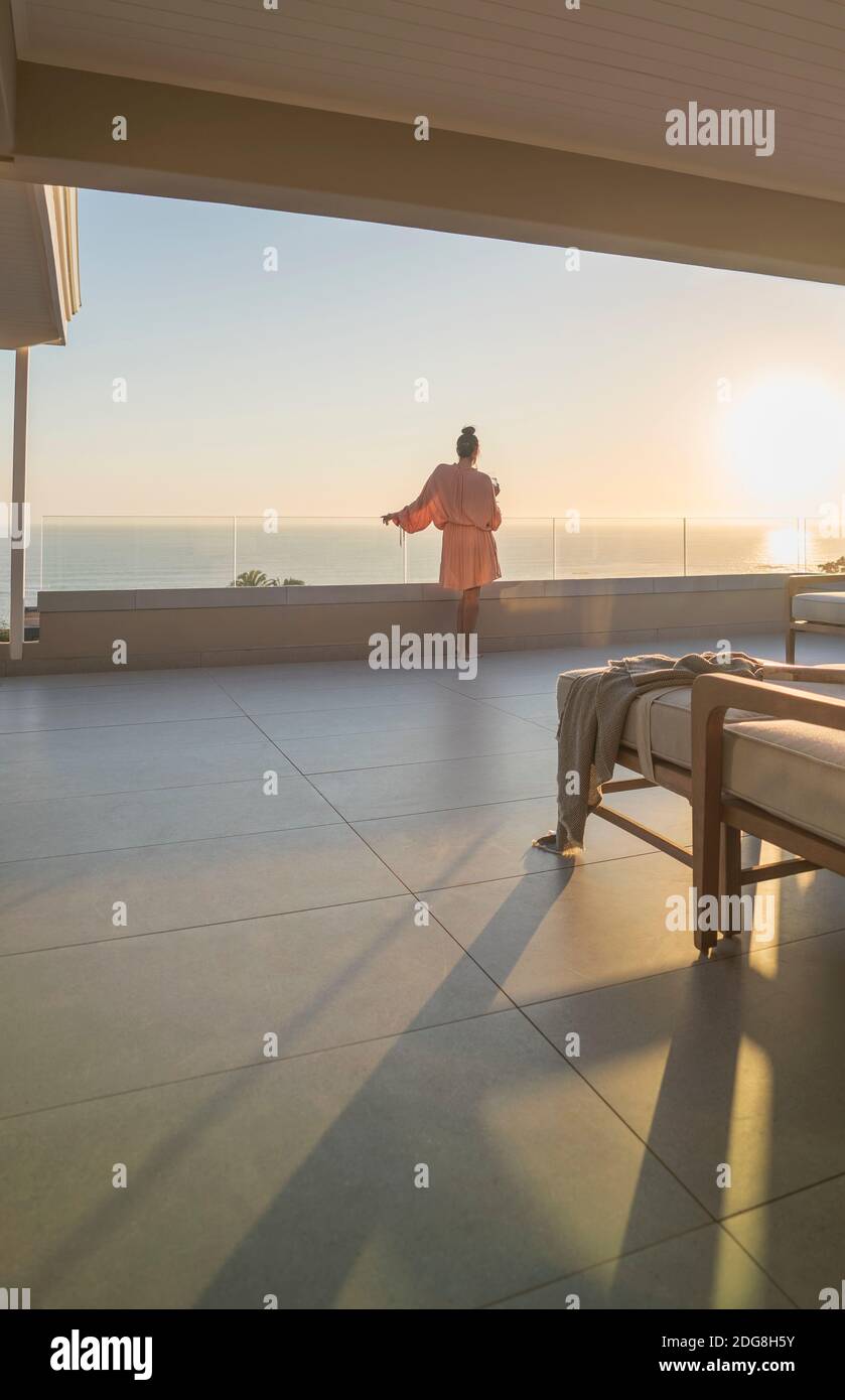 Woman in bathrobe enjoying ocean sunset view from luxury balcony Stock Photo