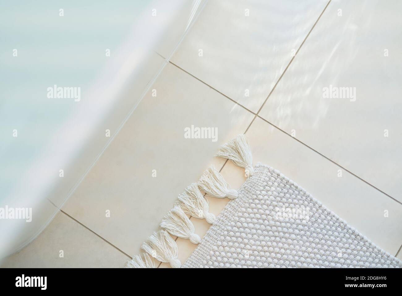 Fringe rug on white tile floor below bathtub in bathroom Stock Photo