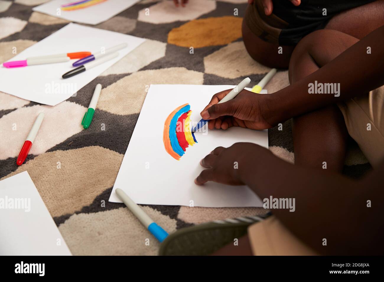 Boy drawing multicolor rainbow with markers on rug Stock Photo