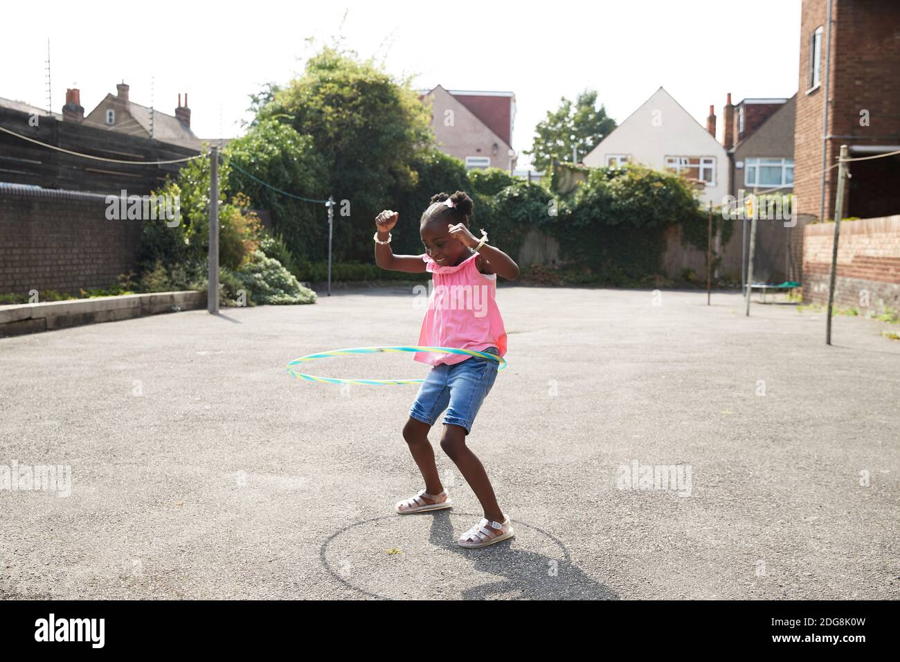 Playful happy girl spinning in plastic hoop in sunny neighborhood Stock Photo