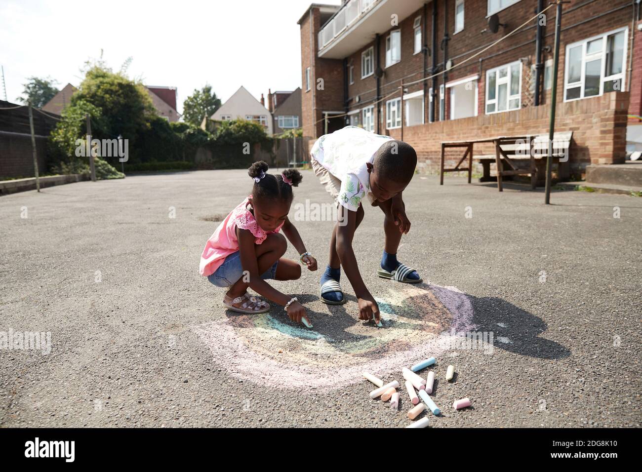 Brother and sister drawing rainbow with sidewalk chalk on pavement Stock Photo
