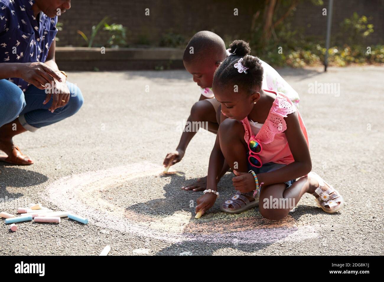 Brother and sister coloring rainbow with chalk on sunny sidewalk Stock Photo