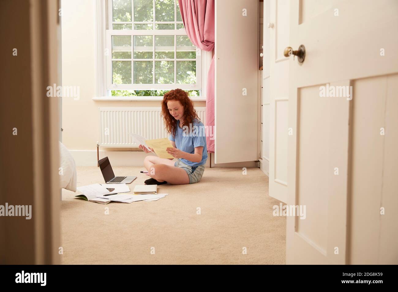 Preteen girl doing homework at laptop on bedroom floor Stock Photo