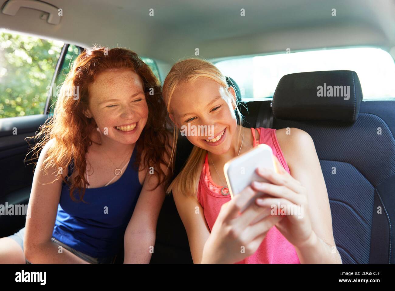 Happy preteen girl friends taking selfie in back seat of car Stock Photo
