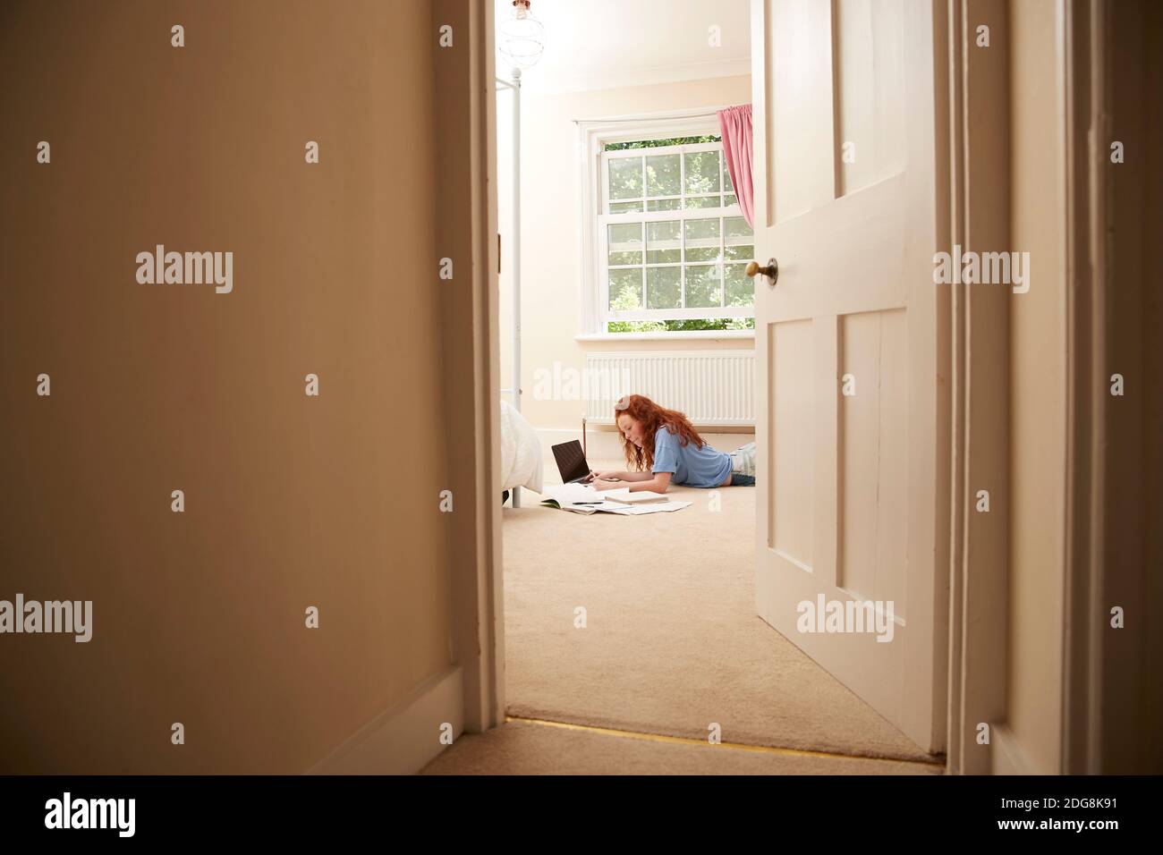 Preteen girl doing homework at laptop on bedroom floor Stock Photo
