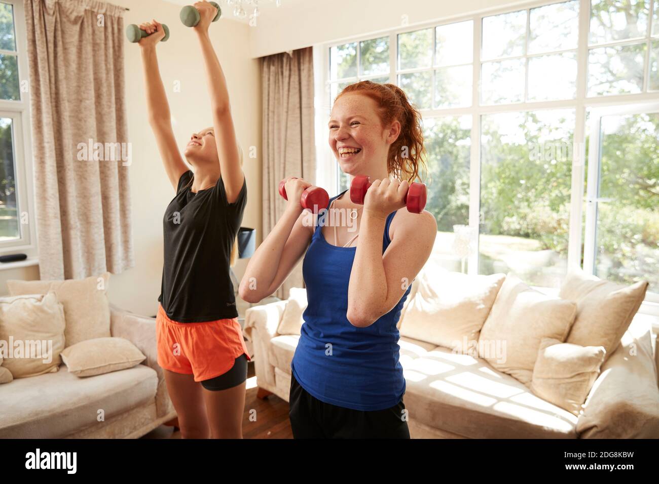 Happy preteen girl friends exercising with dumbbells in living room Stock Photo